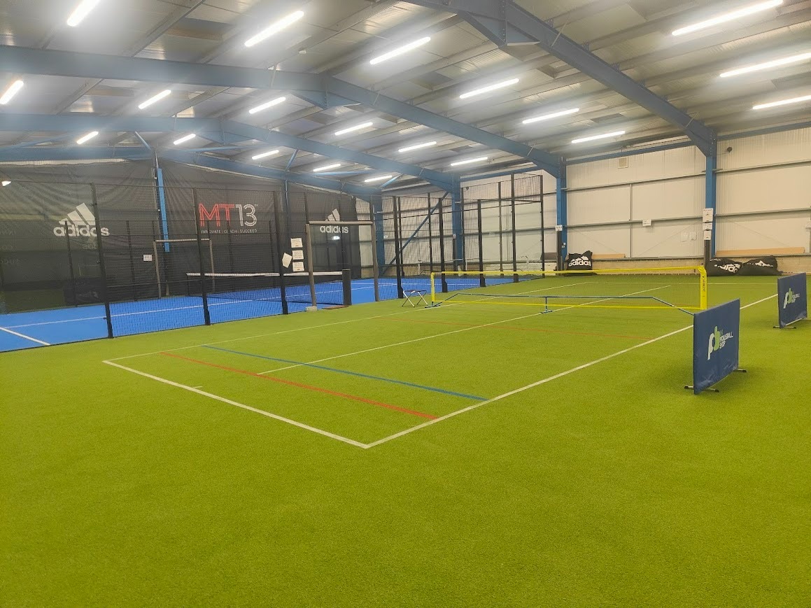 The main hall at The Rally Hub, showing multi-use courts on green Tiger Turf beside an enclosed padel court
