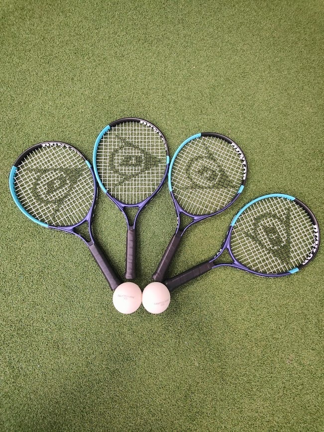 Four hire rackets and two balls laid out on the green Tiger Turf court surface